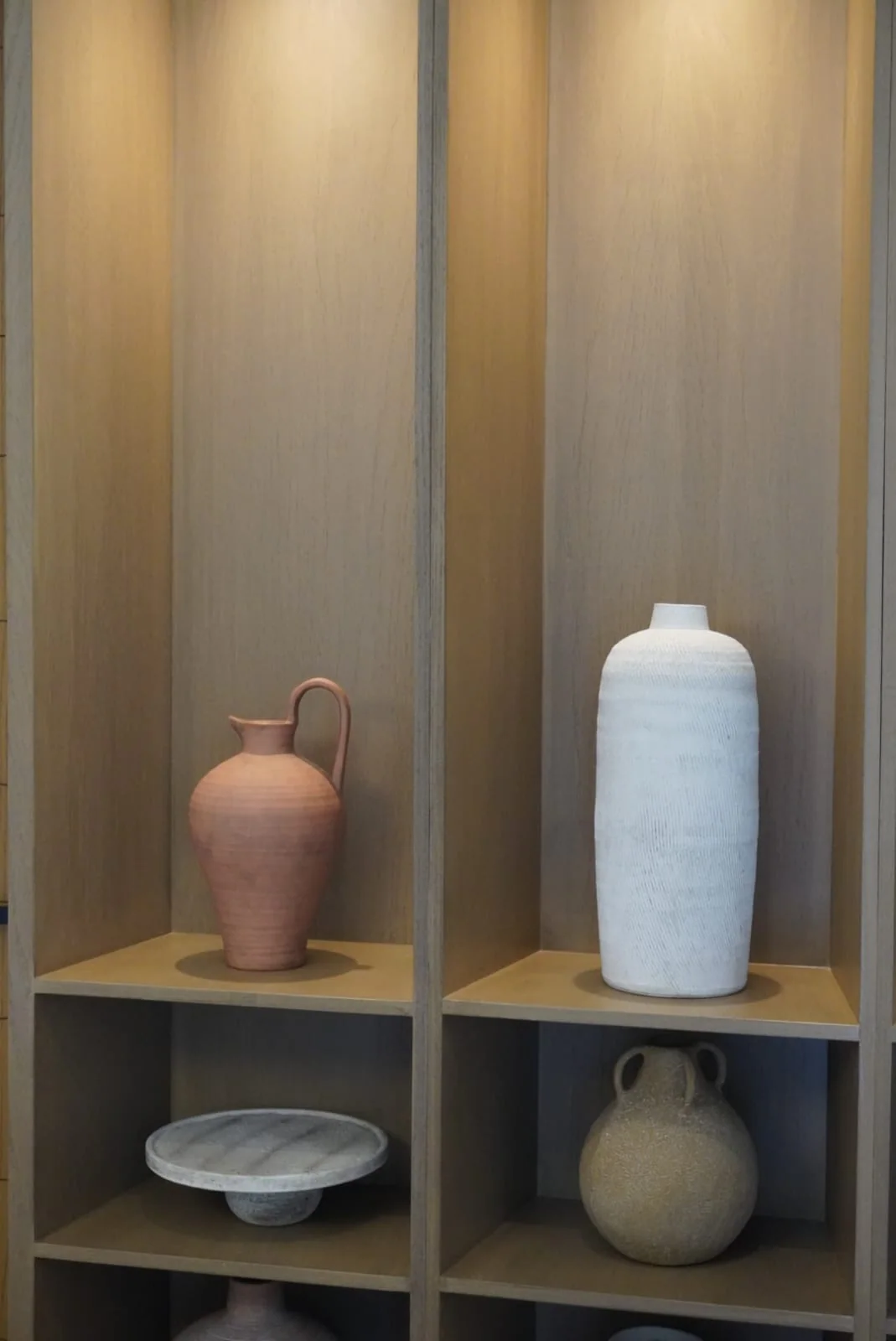 Jarrones de cerámica rosa y blanca en una estantería de madera con luz cálida.